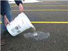 Person pouring a bucket of water on a porous parking lot